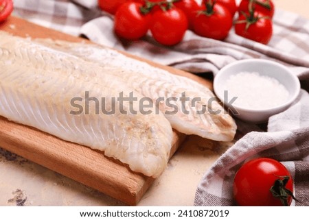Wooden board with raw codfish fillet on beige background