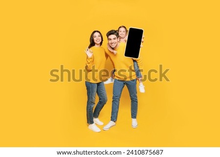 Full body top view young happy parent mom dad with child kid girl 7-8 years old wear pink casual clothes hold use blank screen mobile cell phone isolated on plain yellow background. Family day concept