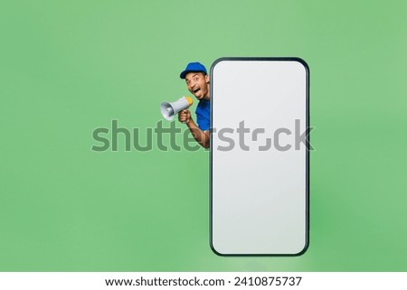 Full body delivery guy employee man wear blue cap uniform workwear work as dealer courier big huge blank screen mobile cell phone scream megaphone isolated on plain green background. Service concept