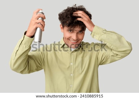 Handsome young man applying hair spray on his curly hair against grey background