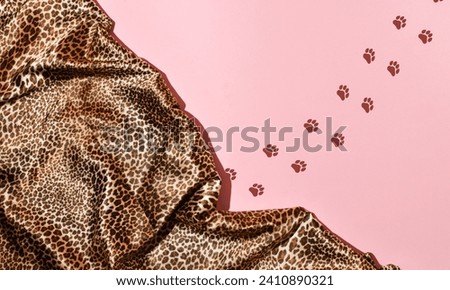 Leopard print satin fabric draped on a pastel pink background, paw print line, creative copy space.