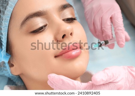 Cosmetologist giving lip injection to young woman in beauty salon, closeup