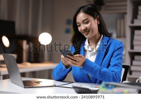 Businesswoman working overtime in the home office is using mobile phone to send messages and chat with colleagues, and analyzing monthly work schedule. Royalty-Free Stock Photo #2410895971
