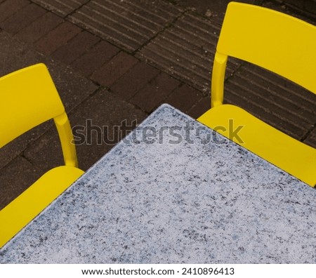 An abstract photograph of an empty table with two yellow chairs