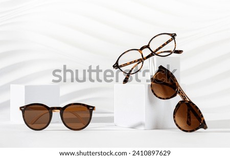 Trendy sunglasses of different design and eyeglasses on podiums on white background. Minimalism. Copy space. Sunglasses and spectacles sale concept. Optic shop promotion banner. Eyewear fashion Royalty-Free Stock Photo #2410897629