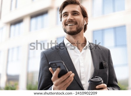 Confident young businessman using cell phone and drinking coffee in the city