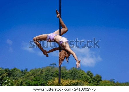 Beautiful Asian girl shows extreme advances by performing pole dance aerial in various positions and spinning stunts on the blue sky around the natural fresh and the waterfall, Concept outdoors.