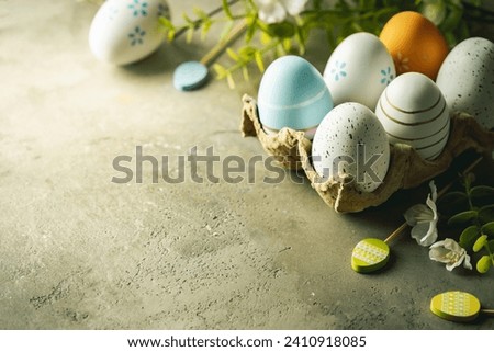 Stylish easter eggs with spring flowers in egg box on gray stone background. Modern easter eggs painted with different colors. Happy Easter