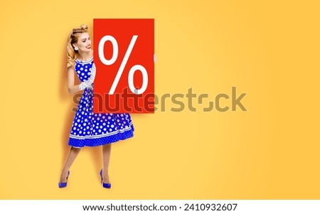 Beautiful woman in pinup dress showing red board with procents % sign. Full body pin up girl holding advertising offer, isolated yellow orange background. Sales, discounts rebates offers ad concept.