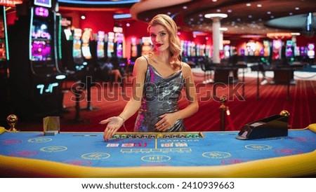 Portrait of a Female Croupier Looking at the Camera and Sharing the Results of a Baccarat Card Game. Beautiful Dealer in the Live Online Video Casino Revealing a Winning Hand Royalty-Free Stock Photo #2410939663