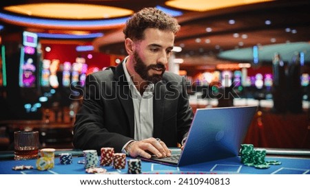 Portrait of a Young Man on Casino Floor, Using Laptop Computer to Play Online Casino Betting Jackpot Games. Professional Businessman Celebrating after Winning Jackpot Bet. Luck and Strategy Royalty-Free Stock Photo #2410940813