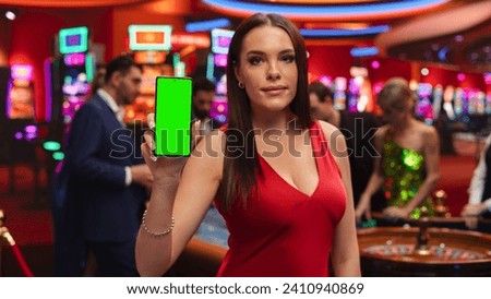Portrait of a Beautiful Caucasian Woman Posing in a Red Dress, Holding a Smartphone with Green Screen Mock Up Display to Use as a Template for a Company Logo or Advertising Call to Action Campaign