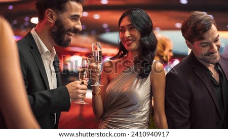 Multiethnic Couple Having a Fun Conversation at a Casino while Drinking Champagne and Gambling at a Roulette Table. Handsome Hispanic Man and Elegant Asian Female Enjoy Nightlife During Their Holiday Royalty-Free Stock Photo #2410940917