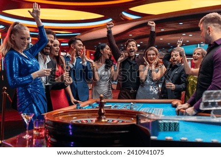 Attractive Multiethnic People Taking Risks and Placing Bets on a Roulette Wheel in a Casino. Croupier Focused on Table with Tokens, while Ball Spins on the Ball Track. Player Celebrates a Winning Bet Royalty-Free Stock Photo #2410941075