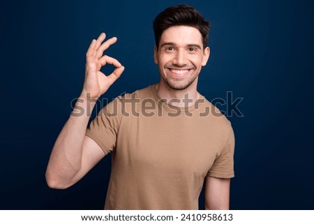 Photo of cheerful handsome pleasant man with bristle dressed beige t-shirt showing okey nice work isolated on dark blue color background