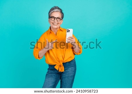 Photo of optimistic elderly business woman proves her new apple iphone is original point finger gadget isolated on cyan color background