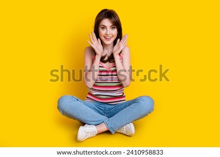 Full size photo of impressed adorable woman dressed knitwear top jeans sit palms near face staring isolated on yellow color background