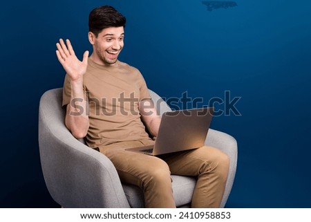 Portrait of nice man with stubble wear beige outfit sit on armchair say hello to laptop on webcam isolated on dark blue color background Royalty-Free Stock Photo #2410958853