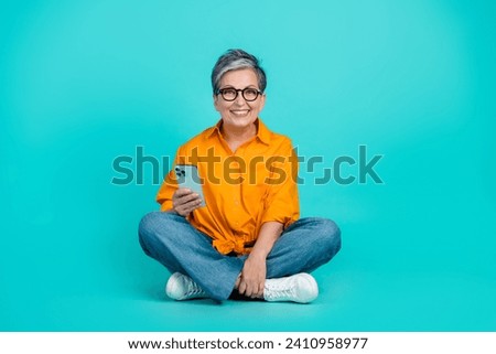Full length body size photo of cheerful grandmother sit floor playing games bet money in casino isolated on aquamarine color background