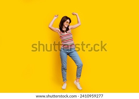 Full body photo of good mood nice girl wear striped tank denim trousers dancing at disco arms up isolated on yellow color background