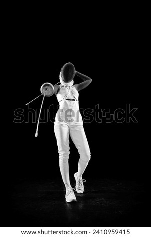 Full length portrait of mastery of sportswoman as she poses with crossed swords, performing confidence and skill against black studio background. Concept of professional sport, championship. Ad