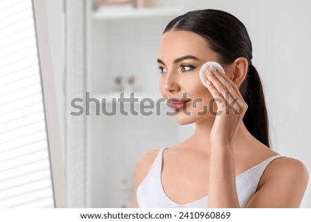 Beautiful woman removing makeup with cotton pad indoors, space for text Royalty-Free Stock Photo #2410960869