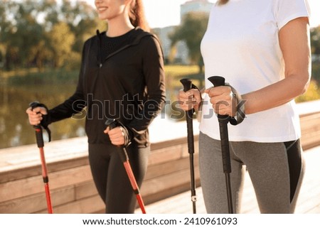 Women practicing Nordic walking with poles outdoors on sunny day, closeup Royalty-Free Stock Photo #2410961093