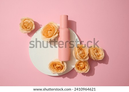 Top view of an unlabeled cosmetic bottle placed on a white round podium with fresh roses on a pink background. Blank labels for typography and branding.