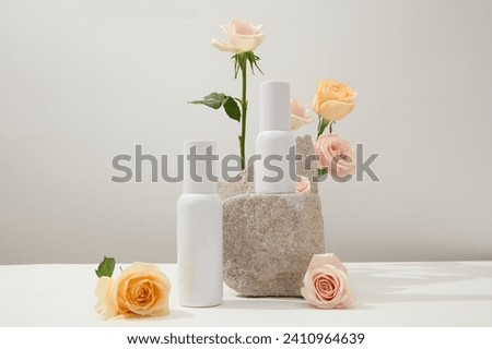 Unlabeled white cosmetics set displayed on a white background with fresh roses and a stone podium. Space with front view for cosmetics advertising. Royalty-Free Stock Photo #2410964639