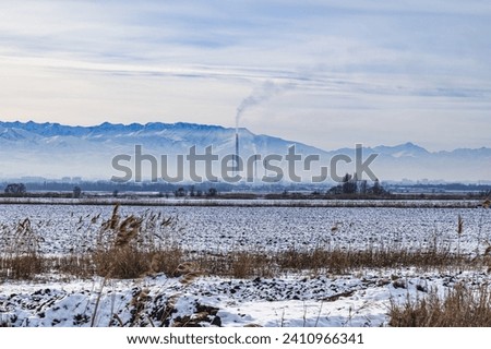 Panorama of a snow-covered mountain valley  and the smoking chimneys of the thermal power plant in the city of Bishkek, Kyrgyzstan. Atmospheric pollution, smog, climate change. Royalty-Free Stock Photo #2410966341