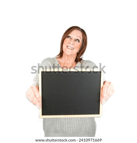 Cute brunette middle aged female teacher holding a blackboard while looking up against a white background