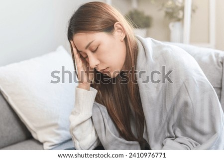 Sick, influenza asian young woman girl headache have fever, hand touching forehead feel unwell, check measure body temperature, illness while sitting rest on sofa at home. Health care people concept. Royalty-Free Stock Photo #2410976771