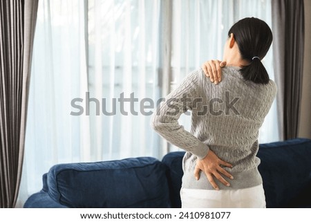 Young woman has problem with structural posture back neck and shoulder pain. Massaged her neck and shoulders for relief. reduce muscle tension on sofa couch in living room Royalty-Free Stock Photo #2410981077
