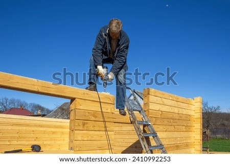 a man builds a wooden house made of profiled timber in the countryside against the blue sky