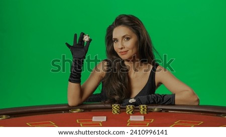 Female in studio on chroma key green screen close up. Woman in black dress sitting at the blackjack poker table smiling holding chip.