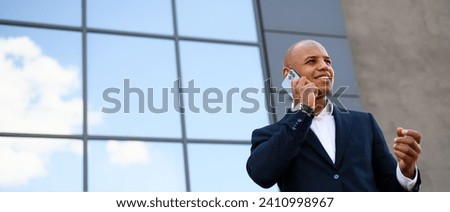 Smiling african american realtor talking on smartphone near building outdoors, banner shot	 Royalty-Free Stock Photo #2410998967