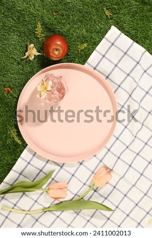 On a green grass background and checkered fabric, pink flowers and pinks dish displayed. Blank space on dish for display product. Top view, picnic on holiday