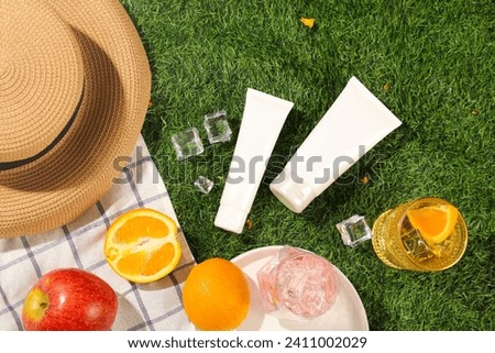 White cosmetic tubes decorated with fruits, cocktail and smoothie cups on checkered fabric and grass background. Mockup tube for cosmetic with space for design packaging. Holiday summer concept