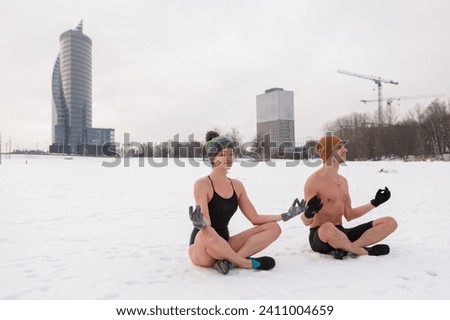 Young couple sitting in yoga at lotus pose after winter sauna. Cold exposure for better health and mood. Swim in ice cold water. Practice to boost immunity. Nordic lifestyle with the urban background Royalty-Free Stock Photo #2411004659
