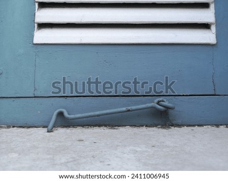 Close up photo of old blue steel window hook on white and blue wooden window. Blurred foreground. 