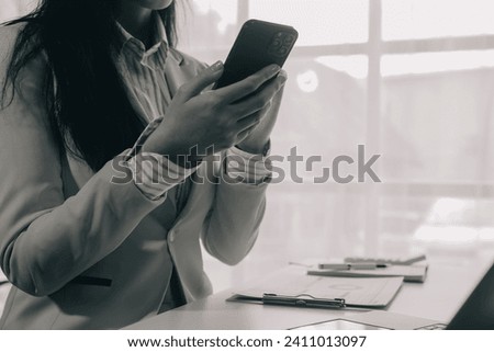 Business woman using mobile phone during working on laptop computer, surfing the internet, searching business data at modern office. Asian businesswoman online working on computer at workplace