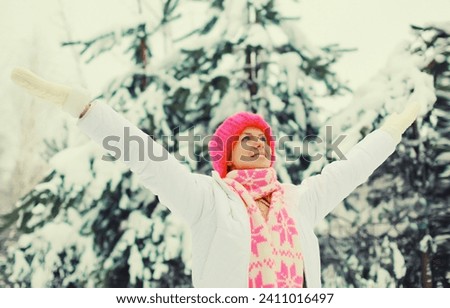 Winter portrait of happy cheerful smiling young woman in colorful knitted hat, scarf enjoys weather on snowy forest park background