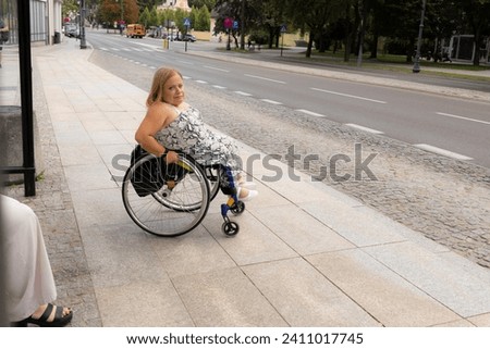 International Wheelchair Day. Person With Short Stature On Wheelchair Waiting For Public Transport On Bus Stop Outdoor. Female Adult With Disability. Copy Space For Text. Transportation Royalty-Free Stock Photo #2411017745