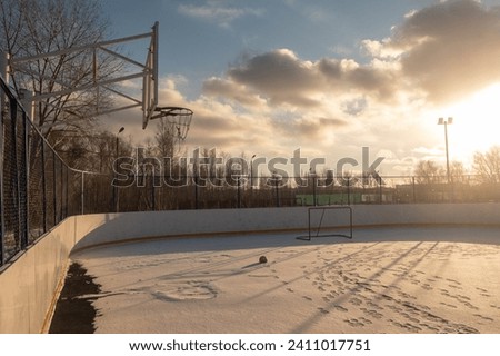 Sports ground with rubber coating covered by snow at the sunset. Basketball hoop with forgotten ball