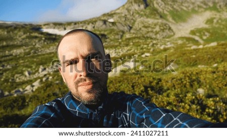 The face of a bearded middle-aged Caucasian man with a short haircut. Against the background of beautiful mountains and blue sky. A travelling blogger taking pictures of himself