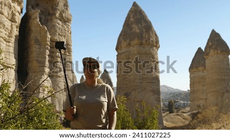 A woman films herself on an action camera against a backdrop of sandstone cliffs. The girl is blogging. Love Valley in Cappadocia. Holidays in Turkey
