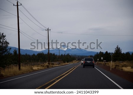several cars drive away on the divided highway towards the snow capped mountain in the distance on a cloudy day