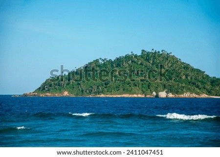 The picture shows a small, mountainous, forest-covered green island surrounded by dark blue ocean and blue sky. Campeche Island, Ilha de Santa Catarina. 