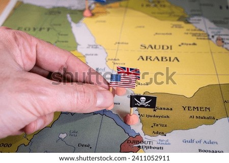 This evocative image captures a hand placing pins adorned with the flags of the USA, UK, and a pirate insignia onto a map of the Red Sea region. It symbolically represents the intricate geopolitical Royalty-Free Stock Photo #2411052911
