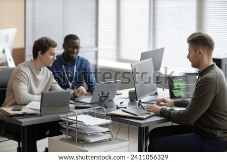 Wide shot of multi-ethnic male IT team working on new cyber security project while sitting at desks of modern company office Royalty-Free Stock Photo #2411056329